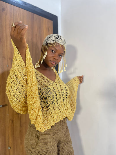 Woman wearing a yellow crochet top and pants against a white wall.