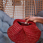 Red crochet held by a hand against a wicker chair and gray cushion background