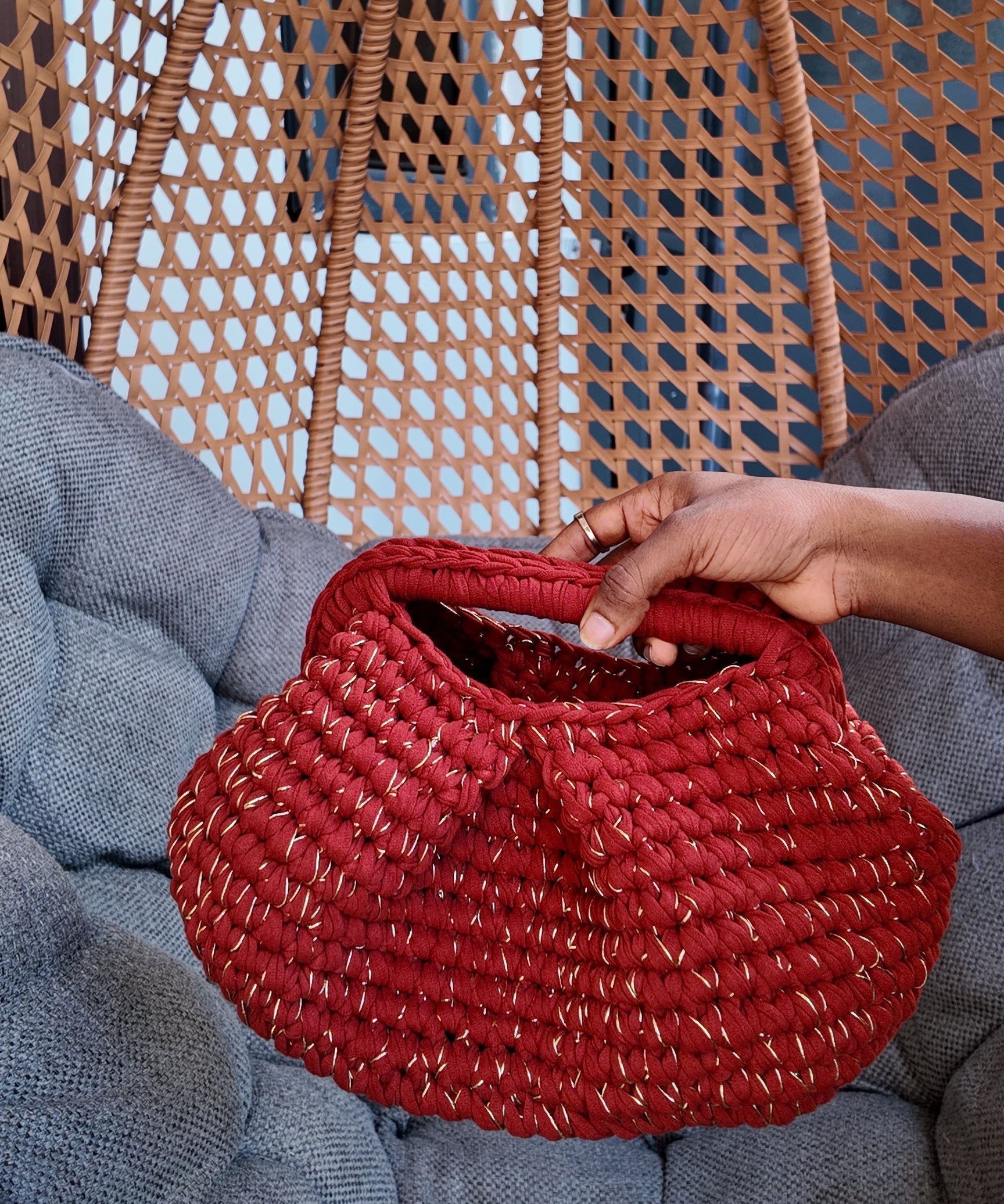 Red crochet held by a hand against a wicker chair and gray cushion background