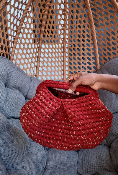 Red crochet held by a hand against a wicker chair and gray cushion background