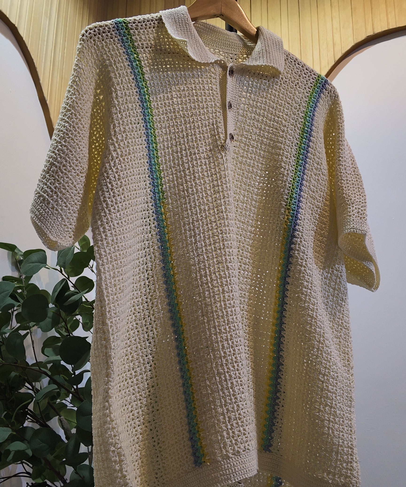 Beige crochet sweater with green accents on a hanger against a neutral background