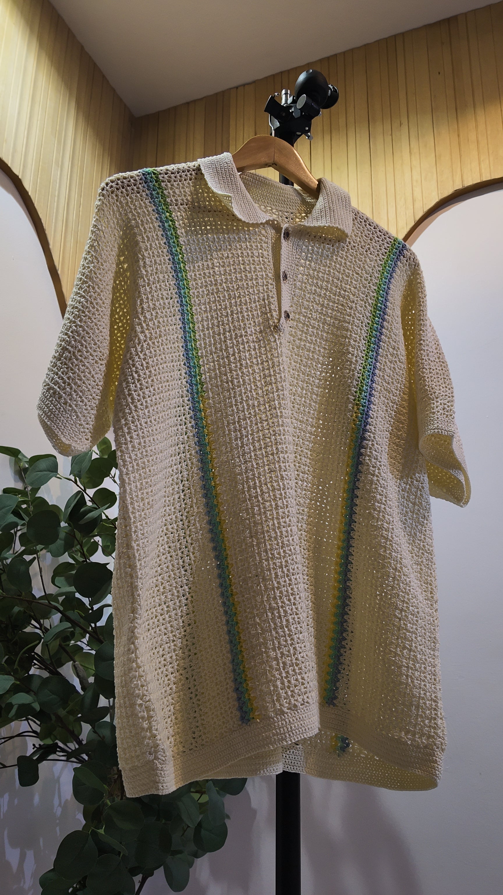 Beige crochet sweater with green accents on a hanger against a neutral background
